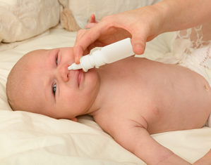 мама распыляет спрей в носу новорожденного