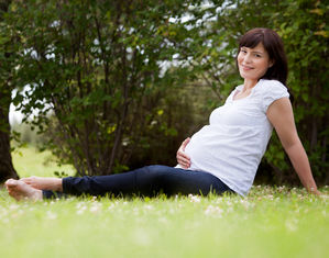 Беременная сидит на траве в парке