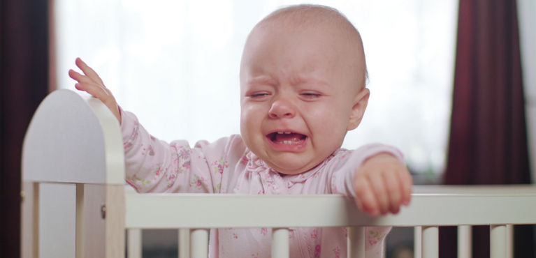 ребенок плачет стоя в кроватке