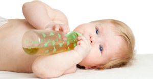 dítě leží na zádech a pije čaj z láhve