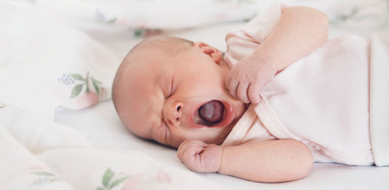 ребенок зевает с сжатыми кулачками