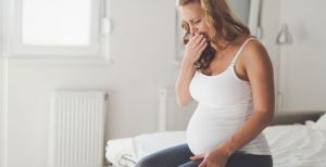 беременная женщина прикрыла рот рукой сидя на кровати 